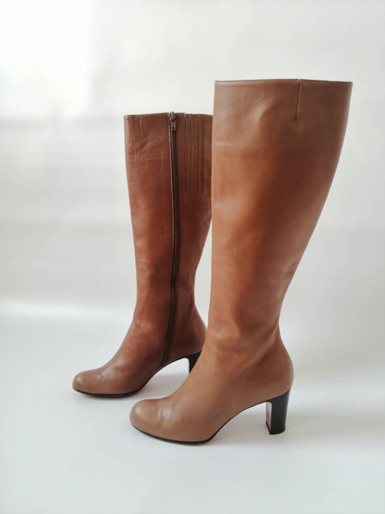 May include: A pair of brown leather knee-high boots with a block heel. The boots have a zipper on the inside of each boot.