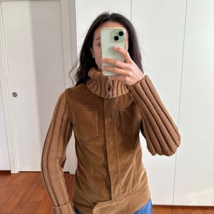 May include: A brown corduroy jacket with a turtleneck collar and knitted sleeves. The jacket has a belt and a zipper closure.