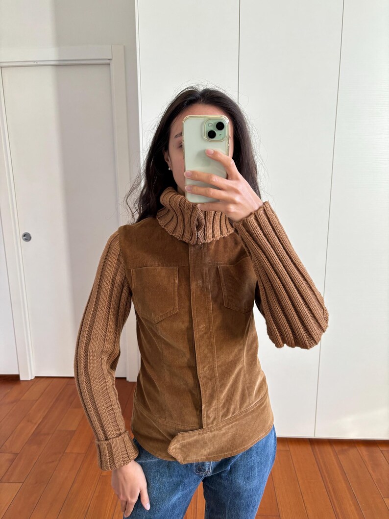 May include: A brown corduroy jacket with a turtleneck collar and knitted sleeves. The jacket has a belt and a zipper closure.