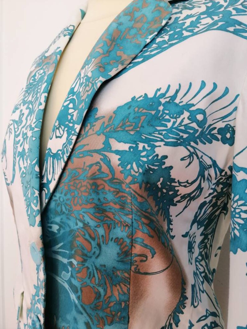 May include: A white blazer with a teal and brown floral pattern. The blazer has a notched collar and a single button closure.