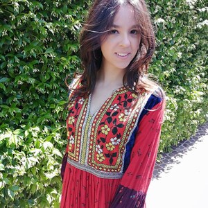 Puede incluir: Una mujer con un vestido rojo de manga larga con bordados coloridos y un estampado floral. El vestido tiene un escote en V y una falda fruncida.