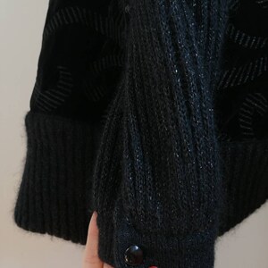 May include: Black knitted cardigan with a velvet panel and a single button closure. The cardigan has a textured knit and a subtle sheen.