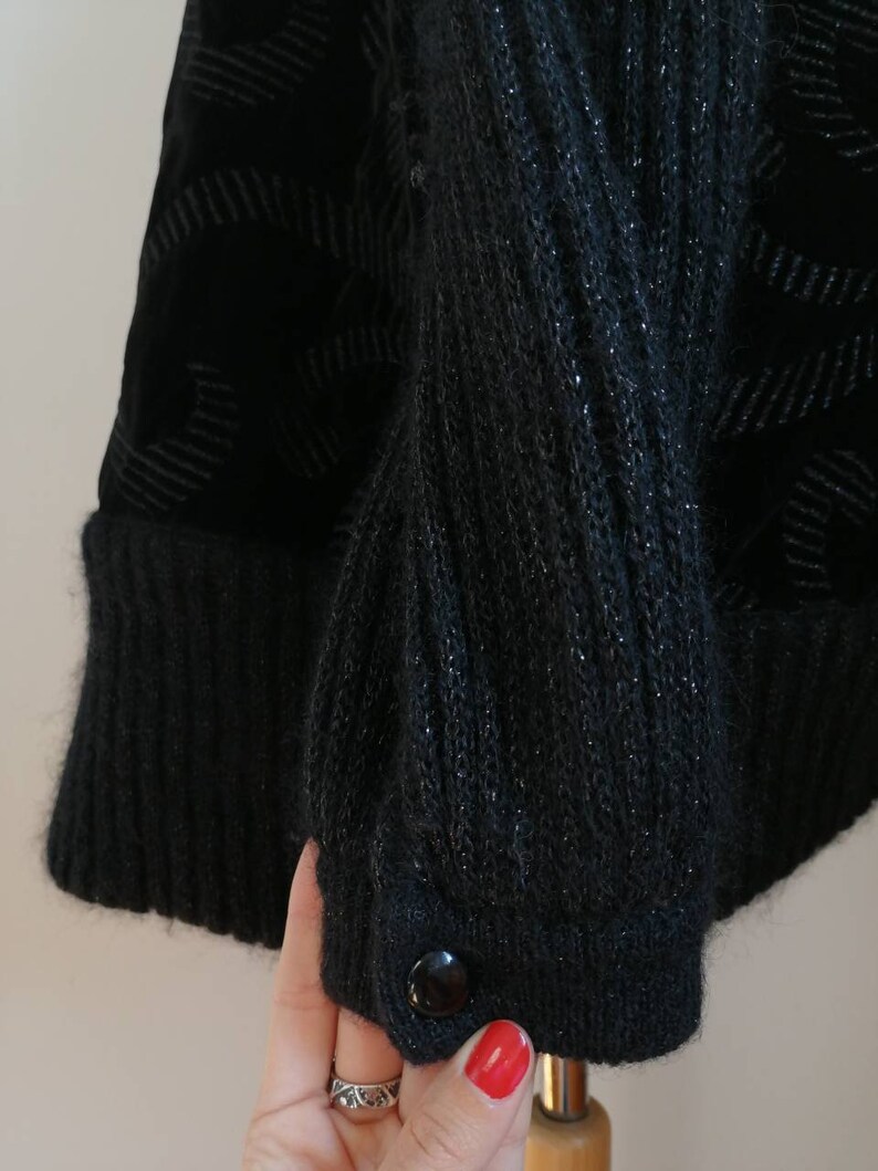 May include: Black knitted cardigan with a velvet panel and a single button closure. The cardigan has a textured knit and a subtle sheen.