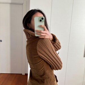 May include: A brown corduroy jacket with a brown knit turtleneck collar and brown knit sleeves. The jacket has a fitted silhouette and a zipper closure.
