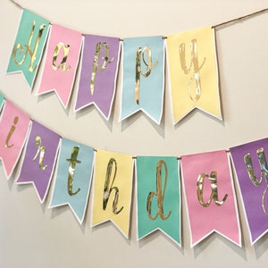 Pu&ograve; includere: Uno striscione color pastello con lettere dorate in foglia d'oro che compongono la scritta "Happy Birthday".
