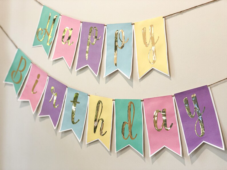 Pu&ograve; includere: Uno striscione color pastello con lettere dorate in foglia d'oro che compongono la scritta "Happy Birthday".
