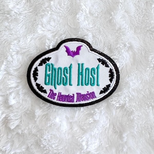 May include: Black and white embroidered patch with a purple bat and the text "Ghost Host The Haunted Mansion" in green and white lettering.