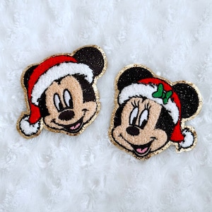 Peut inclure: Deux patchs en feutre de Mickey Mouse sur le thème de Noël. Les patchs sont dorés et rouges avec des accents blancs. Les personnages portent des bonnets de Père Noël.