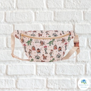 May include: A light pink fanny pack with a repeating pattern of cartoon characters. The bag has a gold zipper and buckle, and a cream-colored adjustable strap. The fanny pack is a fun and functional accessory.