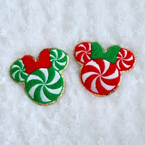 May include: Two red and green candy cane Mickey Mouse head shaped felt patches. The patches are embroidered with a swirl pattern and have a gold outline.