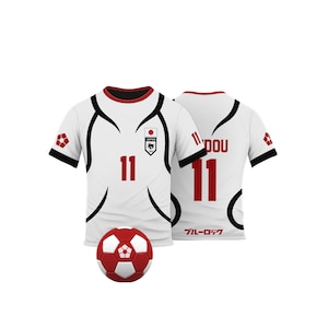K&ouml;nnte beinhalten: Wei&szlig;es Fu&szlig;balltrikot mit roten und schwarzen Akzenten, das die Nummer 11 in Rot zeigt. Das Trikot hat ein japanisches Flaggenemblem und das Wort "JAPAN". Ein rot-wei&szlig;er Fu&szlig;ball liegt vor dem Trikot.