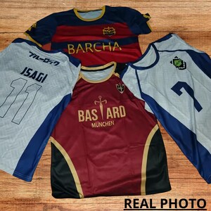 May include: Three soccer jerseys with different designs. The first jersey is white with blue accents and the text "ブルーロック" and "ISAGI" on the front. The second jersey is red with gold accents and the text "BARCHA" on the front. The third jersey is white with blue accents and the text "BASTARD M&Uuml;NCHEN" on the front.