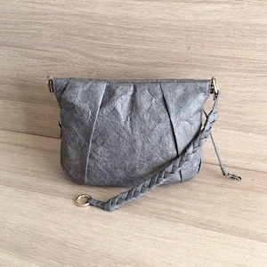 May include: A gray leather shoulder bag with a braided strap and a gold ring detail.