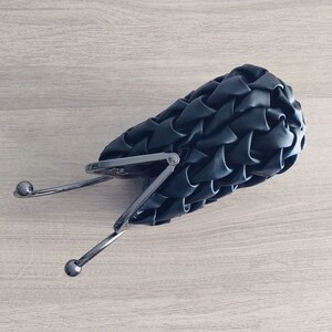Puede incluir: Un bolso de mano negro tejido con cierre de broche plateado y asa de cadena plateada.