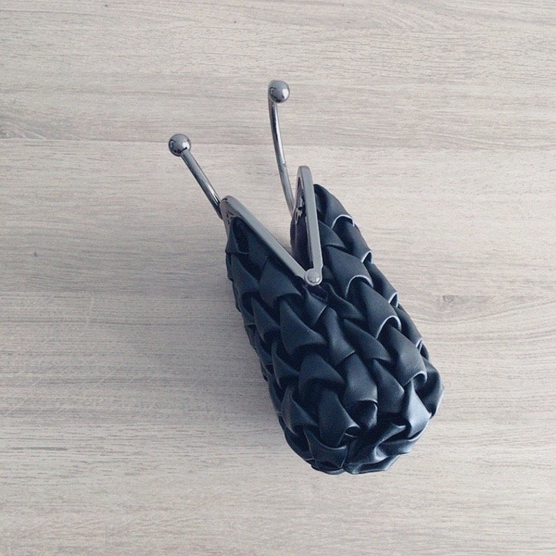 Puede incluir: Un bolso de mano negro tejido con cierre de broche plateado y asa plateada.