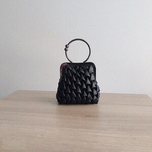 Puede incluir: Un peque&ntilde;o bolso tejido negro con un asa de anillo de plata.