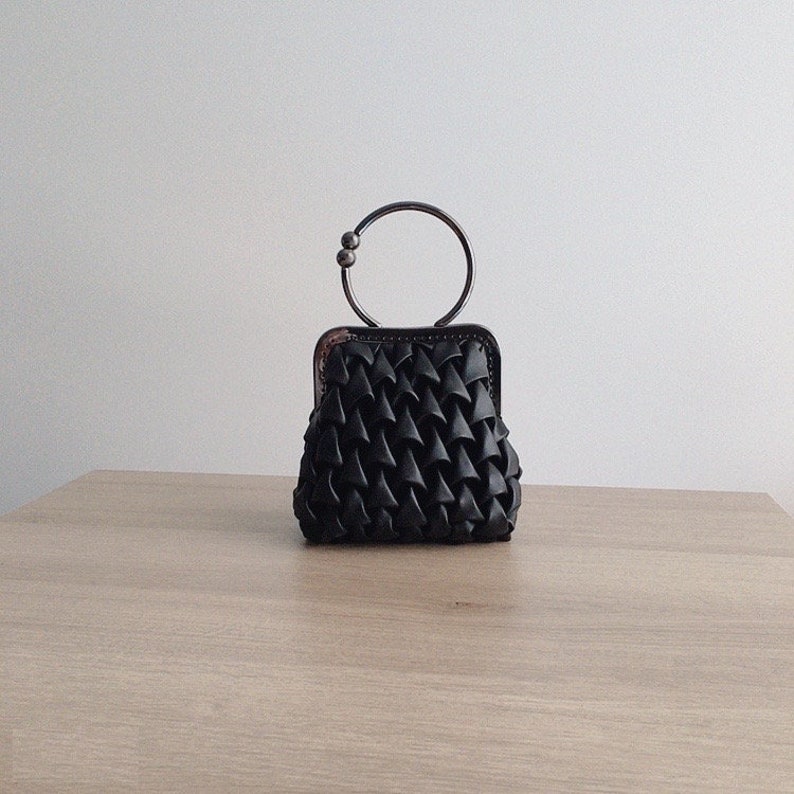 Puede incluir: Un peque&ntilde;o bolso tejido negro con un asa de anillo de plata.
