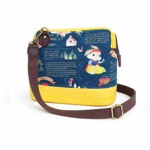 Può includere: Borsa a tracolla gialla e blu con cinturino marrone. La borsa presenta un design a tema Biancaneve con un personaggio coniglio, testo e illustrazioni. La borsa ha una forma rettangolare e una chiusura a zip.