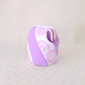 Puede incluir: Una bolsa de cremallera con estampado morado y blanco con un tirador de cremallera dorado.