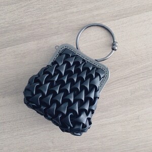 Puede incluir: Un bolso tejido negro con un asa de anillo de plata. El bolso tiene un dise&ntilde;o acolchado texturizado.