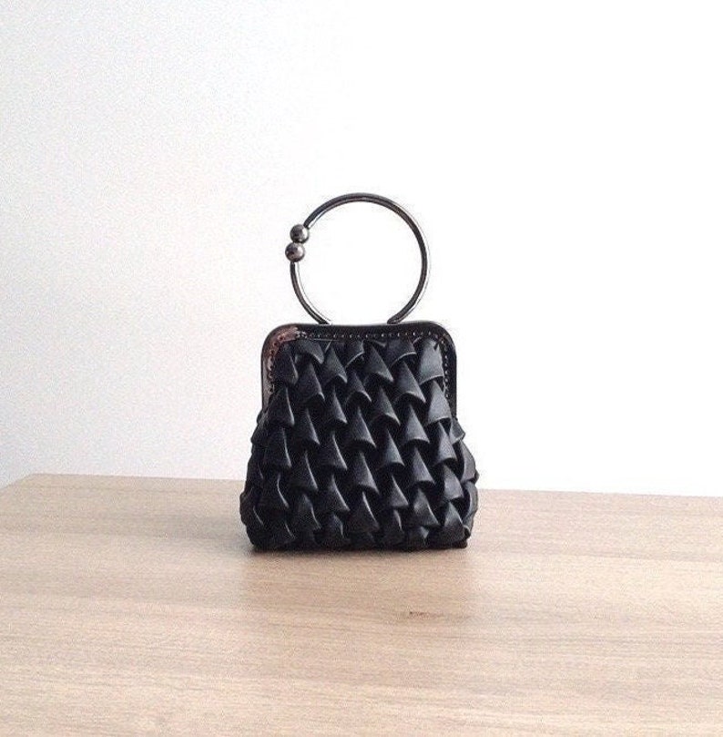 Puede incluir: Un bolso de mano negro texturizado con un asa de anillo de plata. El bolso tiene un dise&ntilde;o geom&eacute;trico &uacute;nico.