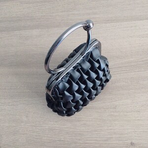 Puede incluir: Un bolso de mano negro tejido con asa de anillo de plata.
