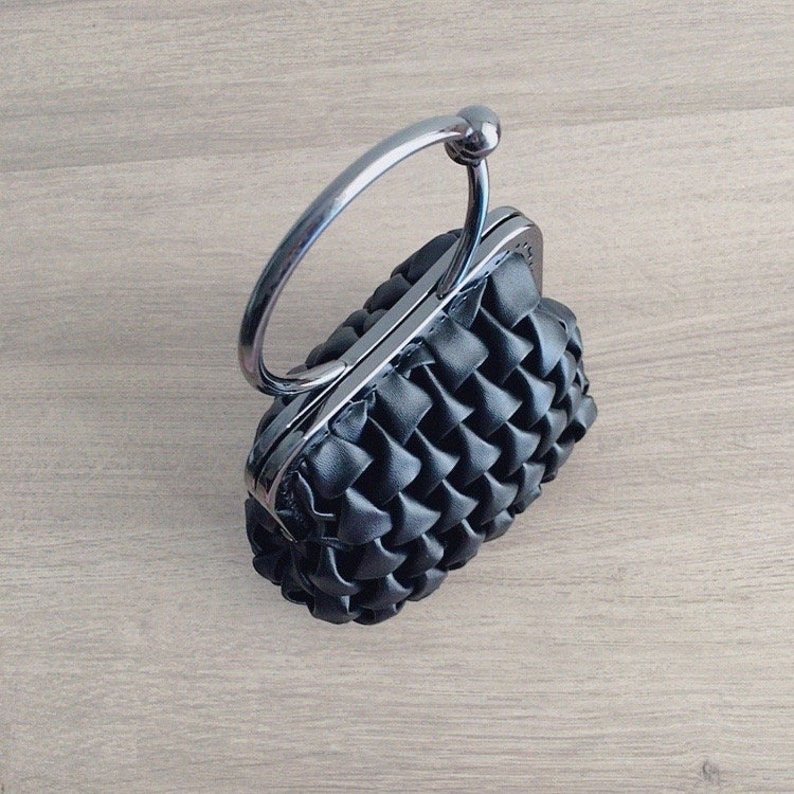 Puede incluir: Un bolso de mano negro tejido con asa de anillo de plata.