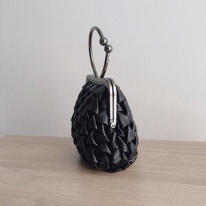 Puede incluir: Un bolso de mano negro acolchado con un asa superior plateada y un cierre de broche.