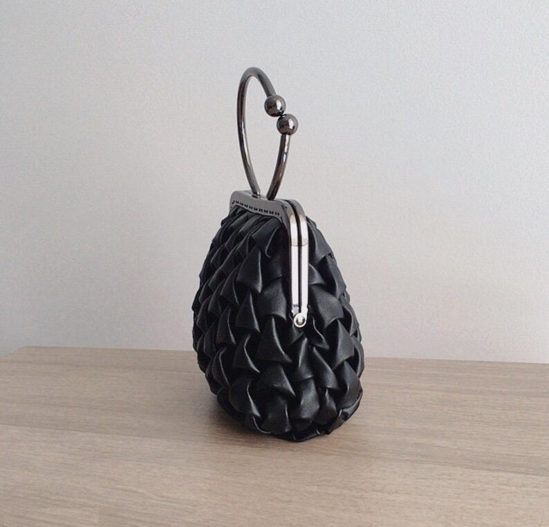 Puede incluir: Un bolso de mano negro acolchado con un asa superior plateada y un cierre de broche.