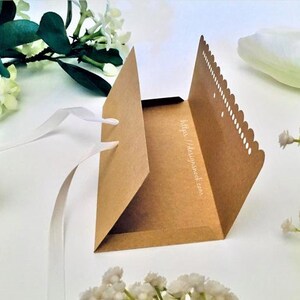 May include: A brown paper envelope with a scalloped edge and a white ribbon tied around it. The envelope is open and the inside is visible. The envelope has the text "https://designsweet.com" printed on the inside.