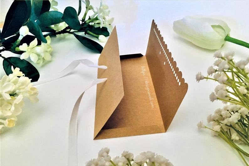 May include: A brown paper envelope with a scalloped edge and a white ribbon tied around it. The envelope is open and the inside is visible. The envelope has the text "https://designsweet.com" printed on the inside.