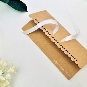 May include: A brown paper envelope with a scalloped edge and a white ribbon tied around it. The envelope has the text "https://designshack.com" printed on the bottom.