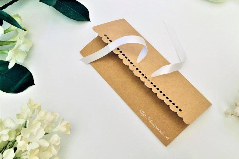 May include: A brown paper envelope with a scalloped edge and a white ribbon tied around it. The envelope has the text "https://designshack.com" printed on the bottom.