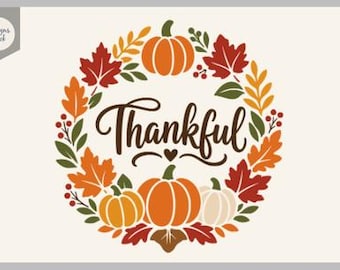 Puede incluir: Una ilustración de corona circular con calabazas naranjas, una calabaza blanca y hojas de otoño en tonos rojos, naranjas y amarillos. La palabra Thankful está escrita en marrón oscuro en el centro, acompañada por un pequeño corazón.