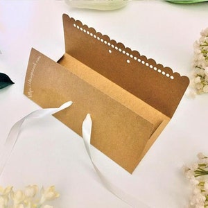 May include: A brown cardboard box with a white scalloped edge and a white ribbon. The box is open and the inside is visible. The box has a website address printed on the front: http://diypapercraft.com.