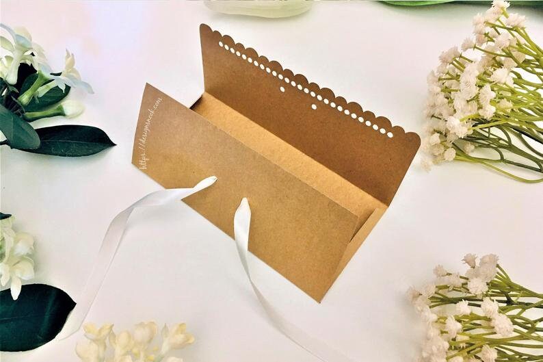 May include: A brown cardboard box with a white scalloped edge and a white ribbon. The box is open and the inside is visible. The box has a website address printed on the front: http://diypapercraft.com.