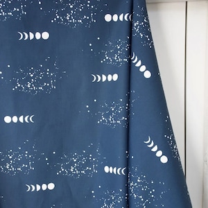 May include: A dark blue fabric with a white moon phases pattern and white speckles. The fabric has the text "100% organic cotton" and "www.mondaluna.com" printed on it.