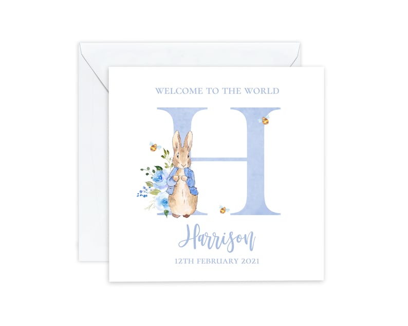 May include: A blue and white baby shower card with a watercolor illustration of Peter Rabbit in a blue jacket. The card features the letter H and the name Harrison with the date 12th February 2021. The text "Welcome to the World" is at the top of the card.
