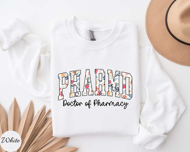 May include: White sweatshirt with the text "PHARMD Doctor of Pharmacy" in black lettering. The word "PHARMD" is decorated with a floral pattern in shades of pink, red, blue, yellow, and green.