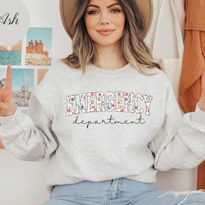 May include: A gray sweatshirt with the text "EMERGENCY department" in white with a floral pattern. The text is in a collegiate font.