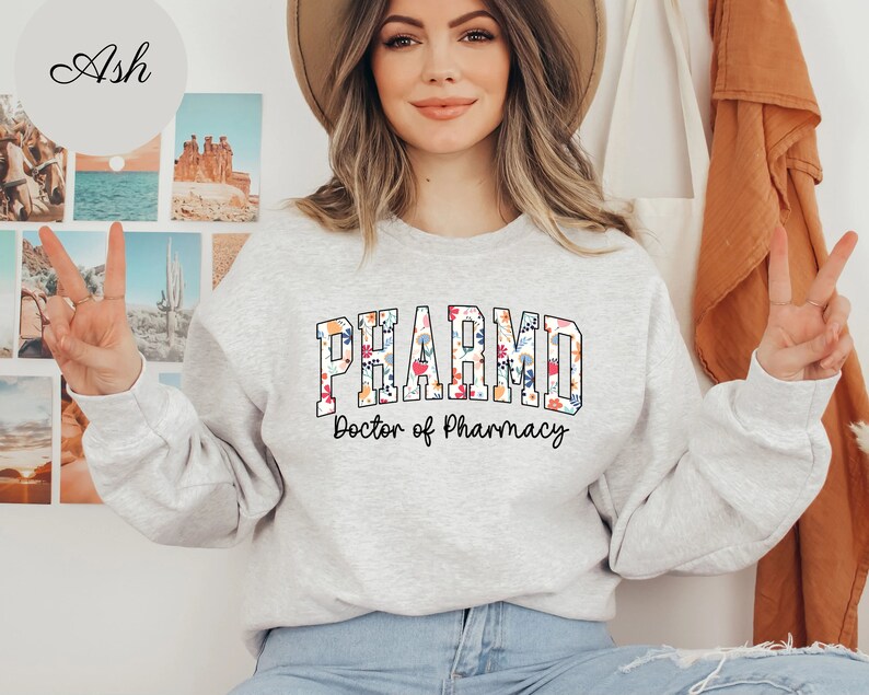 May include: A gray sweatshirt with a floral design that says "PHARM.D. Doctor of Pharmacy" in a collegiate font.