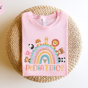 May include: Pink t-shirt with a rainbow and animals around it. The text "PEDIATRICS" is below the rainbow.