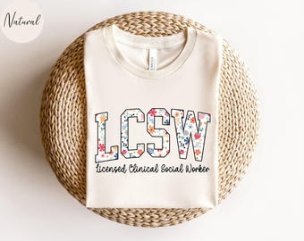 Könnte beinhalten: Ein weißes T-Shirt mit dem Aufdruck "LCSW Licensed Clinical Social Worker". Die Buchstaben sind mit einem floralen Muster in den Farben Rosa, Rot, Blau und Gelb gefüllt.