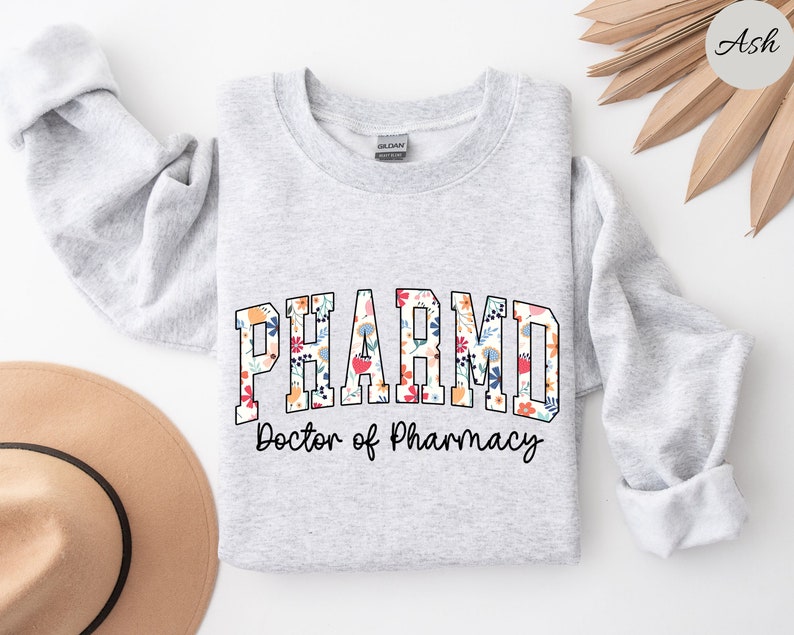 May include: A gray sweatshirt with the text "PHARM.D. Doctor of Pharmacy" in a floral font. The text is in a collegiate style.