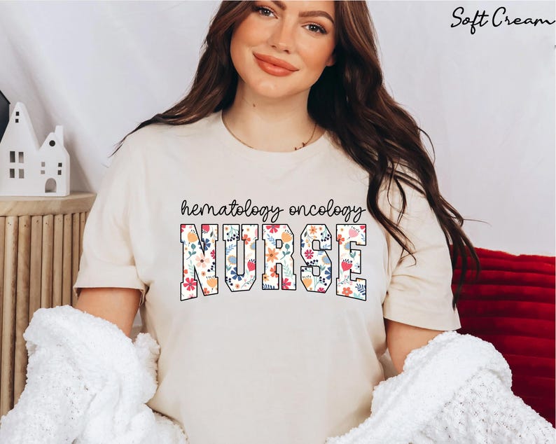 Puede incluir: Una camiseta de color crema con el texto "hematology oncology NURSE" en negro con detalles florales.