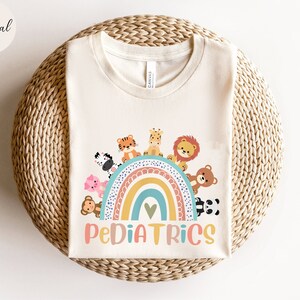 May include: A white t-shirt with a rainbow and animals on it. The rainbow has a heart in the middle and the text "PEDIATRICS" is below it.