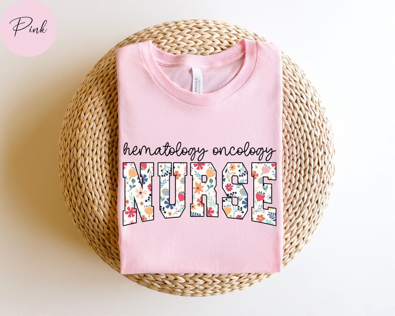 Puede incluir: Camiseta rosa con un dise&ntilde;o floral que dice "hematolog&iacute;a oncolog&iacute;a enfermera" en texto negro.