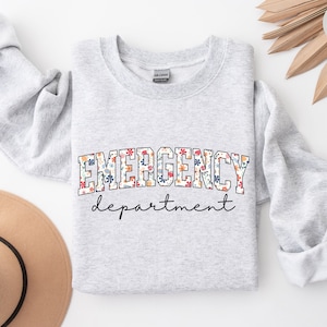 May include: A gray sweatshirt with the text "EMERGENCY department" in white letters outlined in black. The word "EMERGENCY" is decorated with a floral pattern.