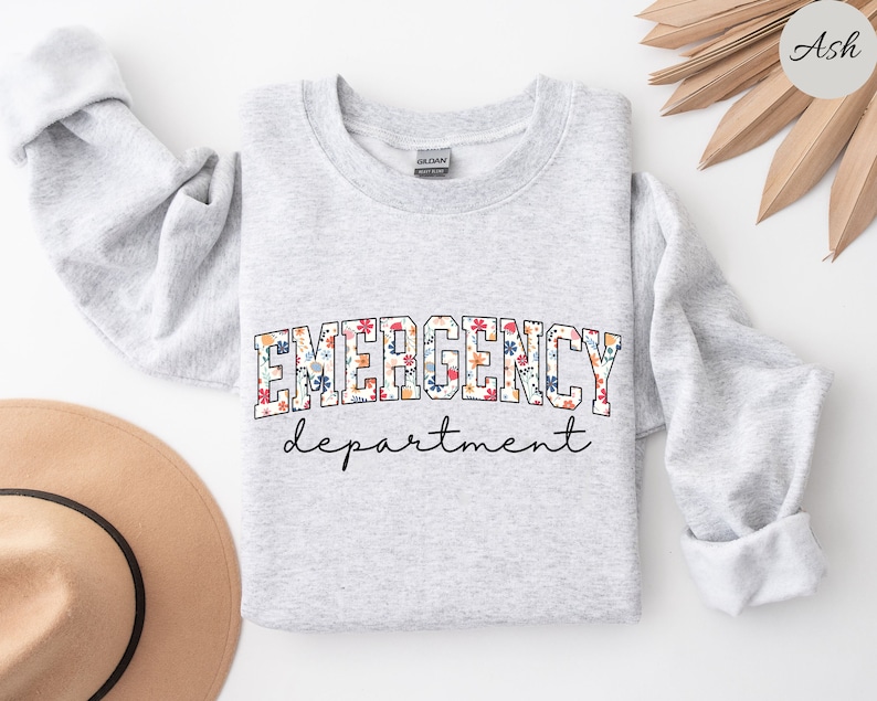 May include: A gray sweatshirt with the text "EMERGENCY department" in white letters outlined in black. The word "EMERGENCY" is decorated with a floral pattern.