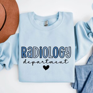 May include: Light blue sweatshirt with the text "Radiology department" in blue and black lettering with a black heart.